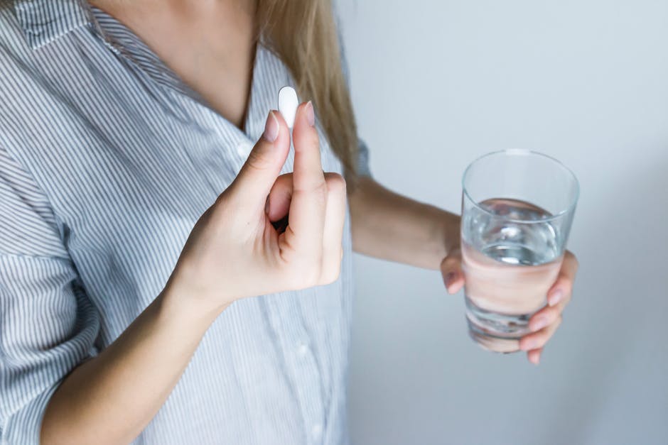 Close-up of a woman holding a pill and a glass of water, ready to take medication. - epämääräiset ruoansulatusvaivat? helikobakteeri