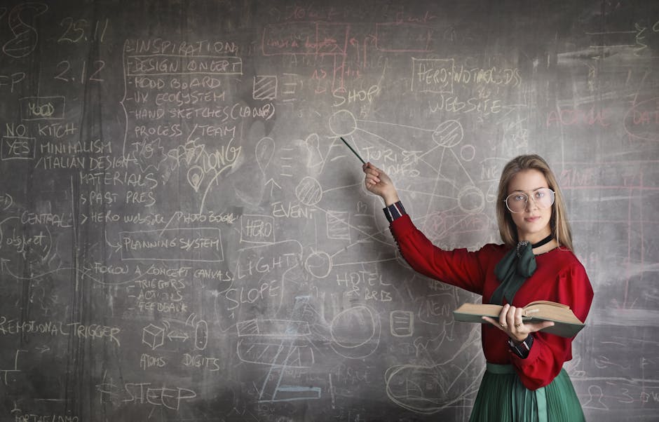Serious female teacher wearing old fashioned dress and eyeglasses standing with book while pointing at chalkboard with schemes and looking at camera - liikunnanopettajan palkka suomessa