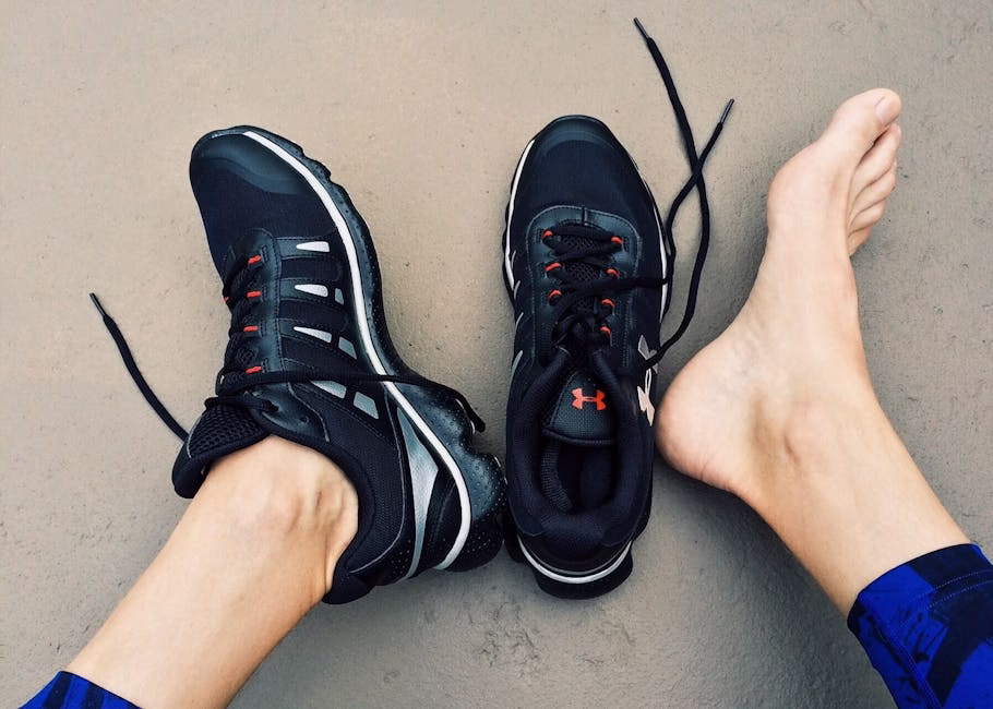 A pair of black sneakers next to bare feet on a gray surface. - miksi jalkoja kuumottaa
